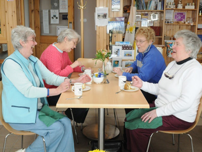 Four older women sitting around café table, laughing