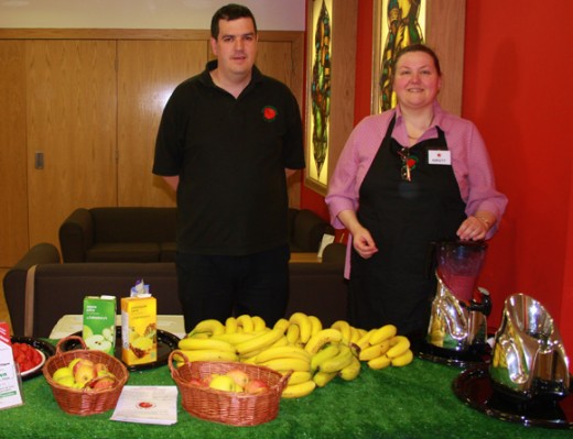 Man and woman behind table displaying bananas and other food